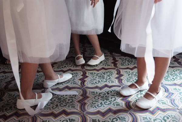 view of the bottom of three flower girls' white dresses and their white shoes as they stand on a colorful tiled floor - photo by Italian wedding photographer JoAnne Dunn